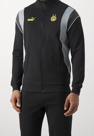 Giacca a track nera con collo alto, chiusura con zip, dettagli grigi, logo PUMA ed emblema del Borussia Dortmund in giallo. Tessuto morbido e elasticizzato.