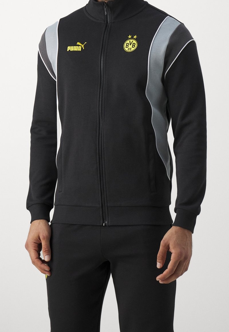 Svart träningsjacka med hög krage, dragkedjestängning, grå detaljer, PUMA-logotyp och Borussia Dortmund-emblem i gult. Mjukt och elastiskt material.