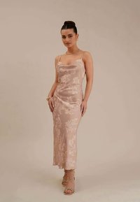 Vestido de seda em rosa suave com padrão floral, alças tipo espaguete e silhueta justa, combinado com sandálias com tiras.