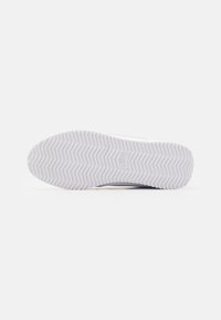 Semelle blanche de basket avec motif de bande de roulement en zigzag et logo Nike embossé au centre sur un fond clair uni.