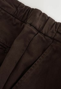 Brauner Cordstoff mit gerippter Textur, ausgestattet mit einem elastischen Bund und seitlichen Nähten, der ein weiches, flexibles Design präsentiert.