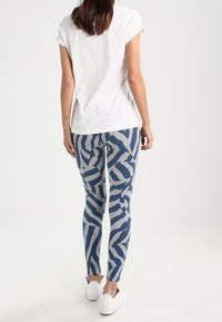 Leggings in un motivo astratto blu e grigio, realizzati in tessuto elastico. Abbinati a una t-shirt bianca a maniche corte e scarpe da ginnastica bianche.