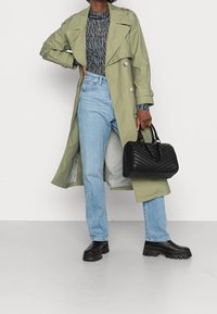 Grønne trenchcoat, mønstret sort langærmet top, lyseblå jeans og sort quiltet håndtaske. Kraftige sorte støvler fuldender looket.