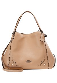 Sac à main en cuir beige Coach avec bords festonnés, ornements floraux et perles, poignée supérieure unique et bandoulière détachable.