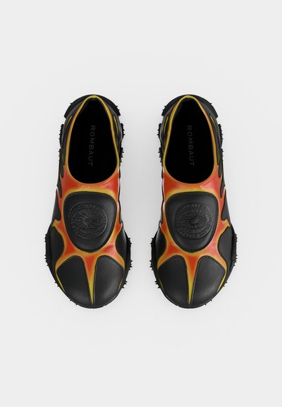 Ζευγάρι μαύρα παπούτσια χωρίς κορδόνια με πορτοκαλί φλογοειδή σχέδια και υφασμένα πέλματα, απόψη σε λευκό φόντο.