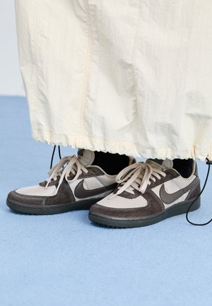 Brune og beige Nike sneakers er lavet af mesh og ruskind, har flade snørrebånd og en sort sål, delvist dækket af et cremefarvet stof.