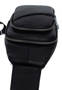 Black leather crossbody bag with two zippered pockets, textured finish, and adjustable strap. Features embossed branding on the front.