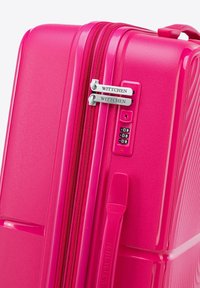 Maleta rígida rosa con superficie texturizada, doble cremallera, candado de combinación y nombre de marca en relieve. Diseño compacto y rectangular.