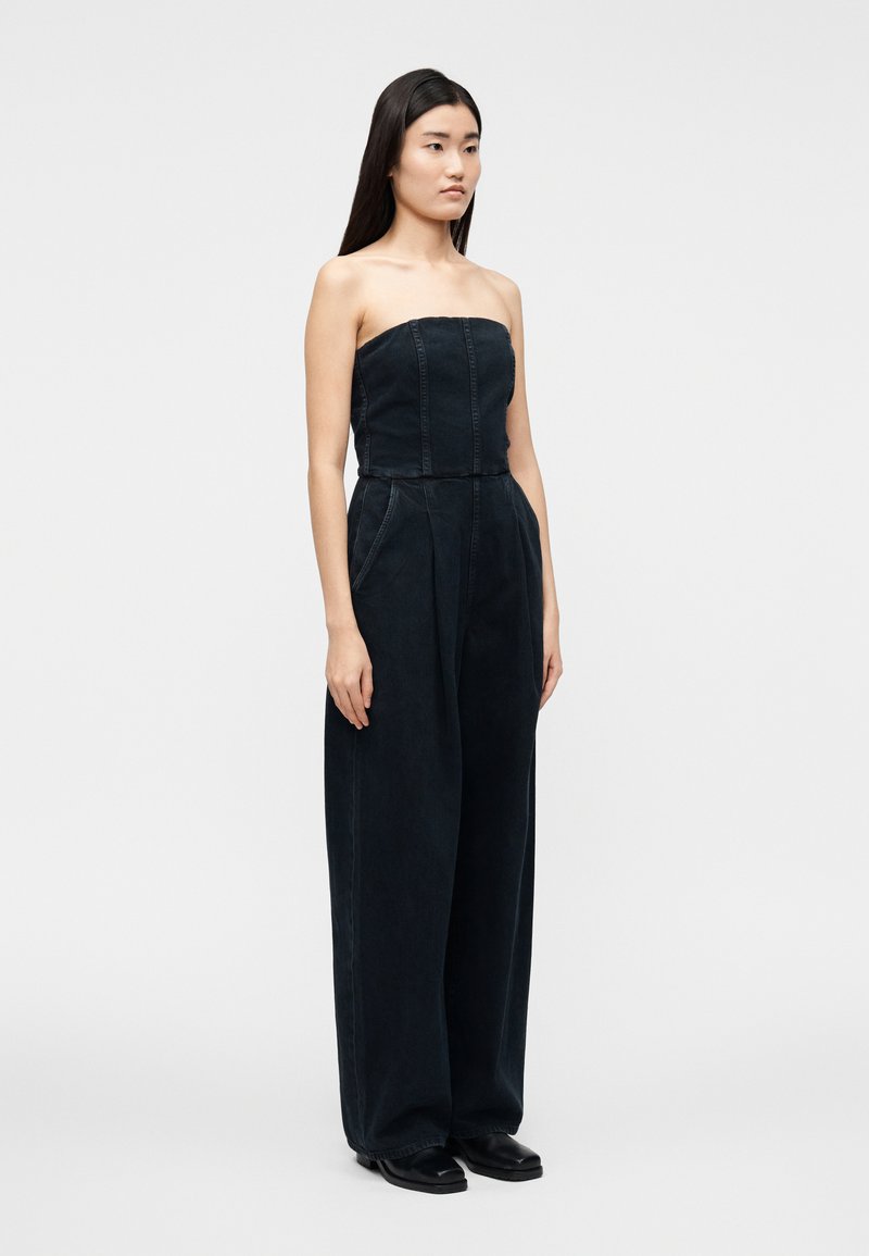 Combinaison en jean sombre sans bretelles avec un corsage ajusté, des jambes larges, des coutures verticales et des poches latérales. Conçue avec des accents minimalistes.