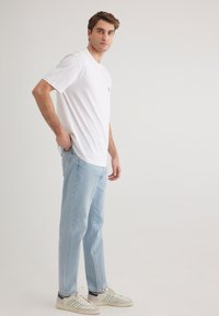 White short-sleeve t-shirt with light blue logo, paired with light blue denim jeans and grey sneakers featuring green accents.
