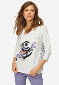 Weißes Langarmshirt mit einem bunten abstrakten Design. Akzente in Lila und Orange, mit blauen Punkten an den Seiten.