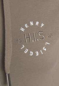 Tan Hoodie mit gesticktem Logo "H.I.S." in Weiß und Grau, dekorativer Naht entlang der Kanten und einer Kordelzugdetails.