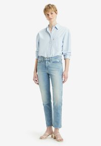 Camisa de botones azul clara con un bolsillo en el pecho, combinada con jeans rectos azul claros y sandalias de tacón blancas con tiras. Diseño simple.