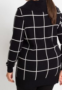 Pull à carreaux noir et blanc avec un col et des poignets côtelés. Design allongé avec une coupe ample, présentant un motif en grille sur tout le tissu.