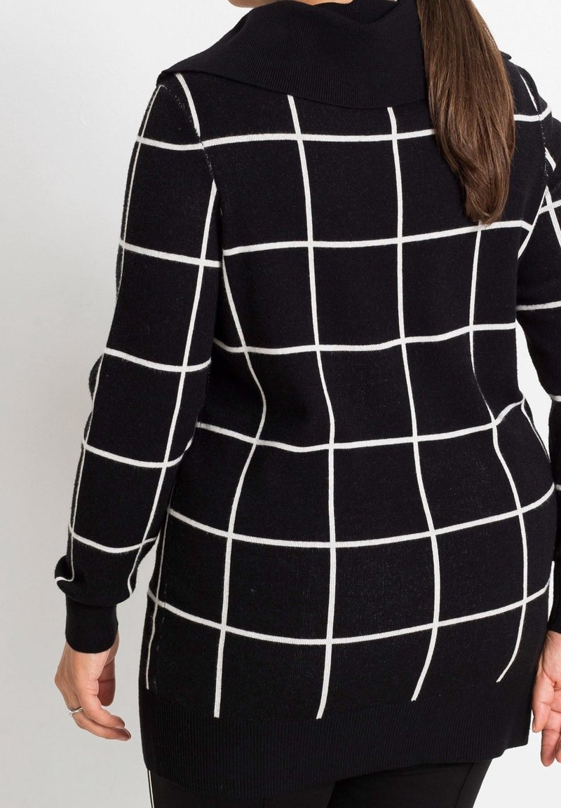 Pull à carreaux noir et blanc avec un col et des poignets côtelés. Design allongé avec une coupe ample, présentant un motif en grille sur tout le tissu.