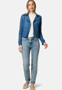 Giacca biker corta in suede blu, top bianco, jeans azzurri chiari, ballerine beige. La giacca presenta cerniere e spalline; i jeans sono attillati con risvolti.