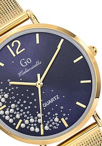 Montre en quartz doré avec un cadran bleu marine, des index heure dorés, des accents scintillants et un bracelet en maille dorée. Design de boîtier rond.