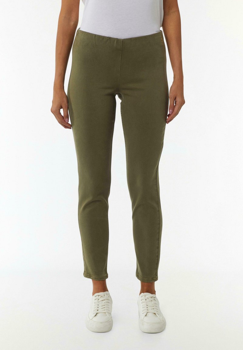 Olijfgroene stretchbroek met een slim fit, met een gladde textuur en zonder zichtbare hardware, gecombineerd met witte sneakers.