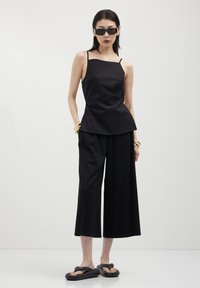 Top nera senza maniche con scollo dritto abbinato a pantaloni neri a gamba larga, entrambi in tinta unita, con design minimale e senza motivi visibili.