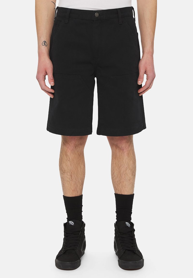 Sorte shorts lavet af slidstærkt stof, med lige pasform, to forlommer og metalknaplukning. Bæres med sorte sokker og sneakers.