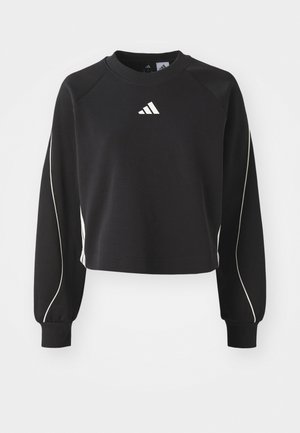 Svart cropped sweatshirt med lange ermer, hvite aksentlinjer på sidene, og en liten hvit logo på brystet. Laget av mykt stoff.