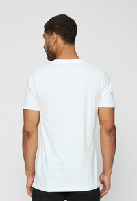 Hvid bomulds t-shirt med korte ærmer, rund halsudskæring og et enkelt design, set fra ryggen. Blød tekstur, ingen synlige mønstre eller detaljer.