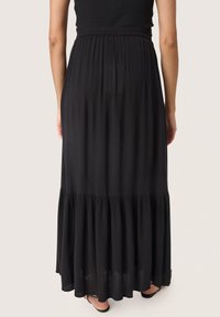 Jupe maxi noire en tissu léger avec une texture plissée et un ourlet en étages, dotée d'une taille élastique et d'un design minimaliste.