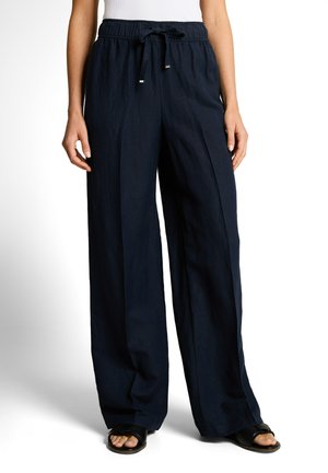 Woman wearing loose dark navy drawstring pants and black open-toe sandals, standing with hands relaxed by sides.