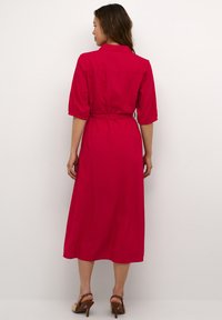 Fuchsia skjortklänning med krage, trekvartslång ärm, midjeband och en flödande A-linjeform. Slät tyg med minimal textur.