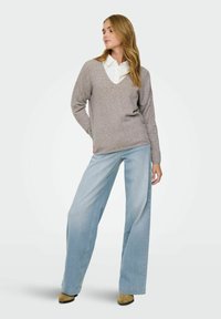Pull en v gris clair à manches longues, associé à un jean bleu clair à jambe large et des bottes à talons beiges. Texture douce, coupe décontractée.