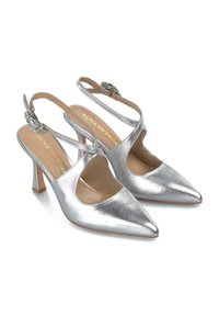 Zapatos de tacón tipo slingback de metal plateado con punteras puntiagudas, diseño lateral recortado y herrajes decorativos en las correas. Tacones de aguja, textura suave.