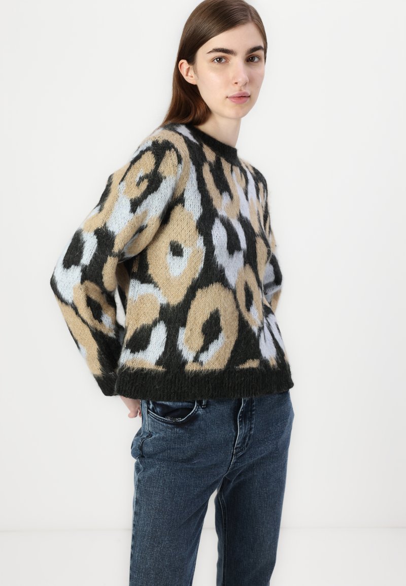 Strickpullover mit einem Leopardenmuster in Beige, Schwarz und Blau, mit Rundhalsausschnitt und lockerer Passform, kombiniert mit dunkelblauen Jeans.