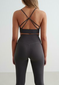 Grijze sportbeha met kruislings rugbanden, gecombineerd met bijpassende hoge taille legging. Gladde textuur, aansluitend ontwerp en geen zichtbare patronen.