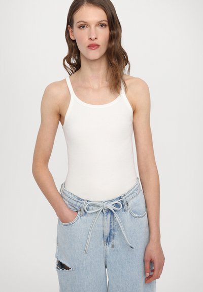 Valkoinen ribbed tank top ohuiden olkahihnojen kanssa, yhdistettynä vaaleansinisiin farkkuihin, joissa on etutai ja kulutuspintaa.