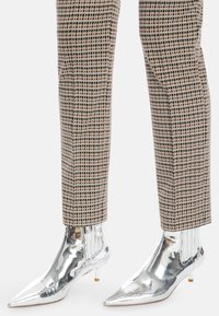 Silberne Lackleder-Stiefeletten mit hohen Absätzen, spitzen Zehen und gefranstem Seitendetail, kombiniert mit karierter Anzughose.