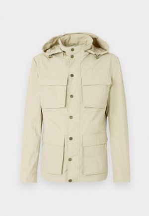 Lyse beige jakke med hette, med to brystlommer og to nedre lommer. Trykknaplukking med en teksturert stofffinish.