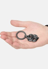 Keychain made of black metal featuring a twisted geometric design and a circular attachment loop, placed in a hand for scale.