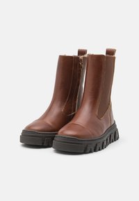 Ruske nahkasaapad ankle sildi tekstuuriga viimistlusega, elastsete külgpaneelidega ja paksu musta kummitaldaga. Omab tugevdatud varba ja kanna aktsente.