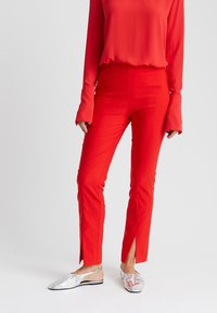 Rode broek met zijopeningen en een gladde textuur, gecombineerd met zilveren platte schoenen. Het bovenstuk heeft lange mouwen en een losse pasvorm.