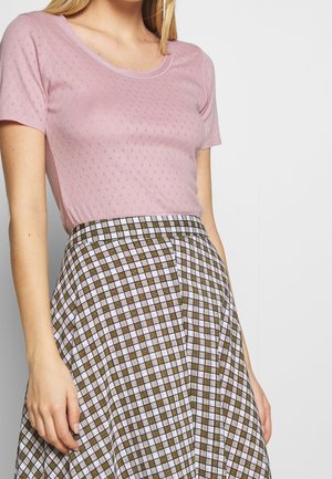 Femme portant un top en maille à manches courtes rose clair à motifs, associé à une jupe taille haute à motif à carreaux marron et blanc.