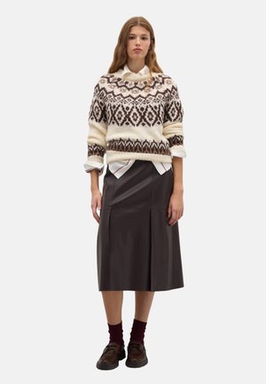 Pull en tricot crème avec des motifs géométriques marron, porté sur une chemise blanche à col. Jupe midi en cuir noir avec des plis et chaussures marron foncé.