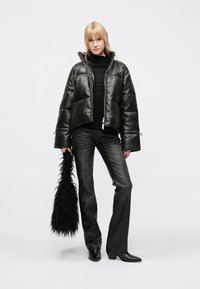 Gepolsterte schwarze Lederjacke mit hohem Kragen, Reißverschlussverschluss und weiten Ärmeln, kombiniert mit dunklen, ausgestellten Jeans und einer langen Pelztasche.