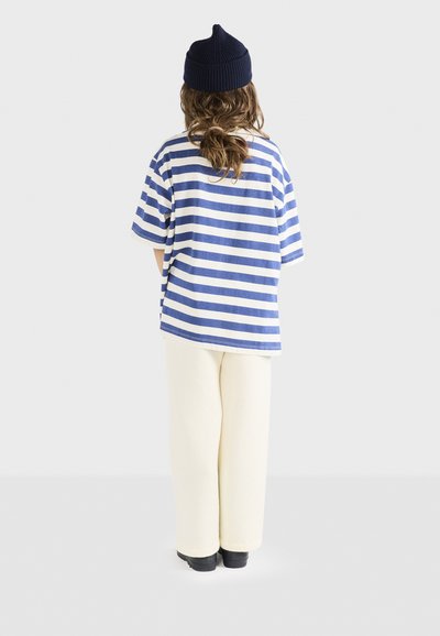 Stribet t-shirt i blå og hvid, løs pasform, parret med off-white brede bukser. Sættet suppleres af en marineblå strik-hue.