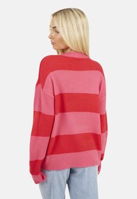 Maglione oversize a righe alternate rosse e rosa. Tessuto morbido con scollatura rotonda e spalle scese. Vestibilità casual e rilassata.
