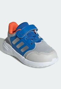 Szaro-niebieski but sportowy z siateczkową cholewką, pomarańczowymi akcentami, szerokim paskiem na rzep oraz białą podeszwą. Trzy szare paski po boku.