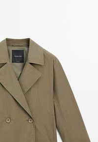 Olivengrüner Doppelreiher-Mantel mit breitem Revers, zwei Knöpfen und glatter Textur. Das Etikett "Massimo Dutti" ist innen am Kragen sichtbar.