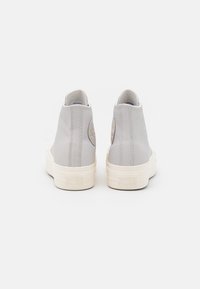 Hoge sneakers van lichtgrijs leer met witte rubberen zolen. De achteraanzicht toont het logo detail en de stiksels nabij de hiel.