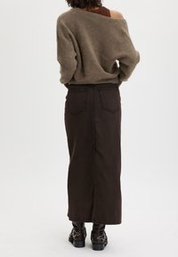 Brun stickad tröja med oversize passform, i kombination med en lång mörkbrun denimkjol med bakfickor och ankelhöga svarta stövlar.