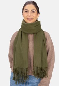 Écharpe vert olive en tissu doux avec bords frangés, drapée autour du cou, complétant un pull marron clair. Design minimaliste.