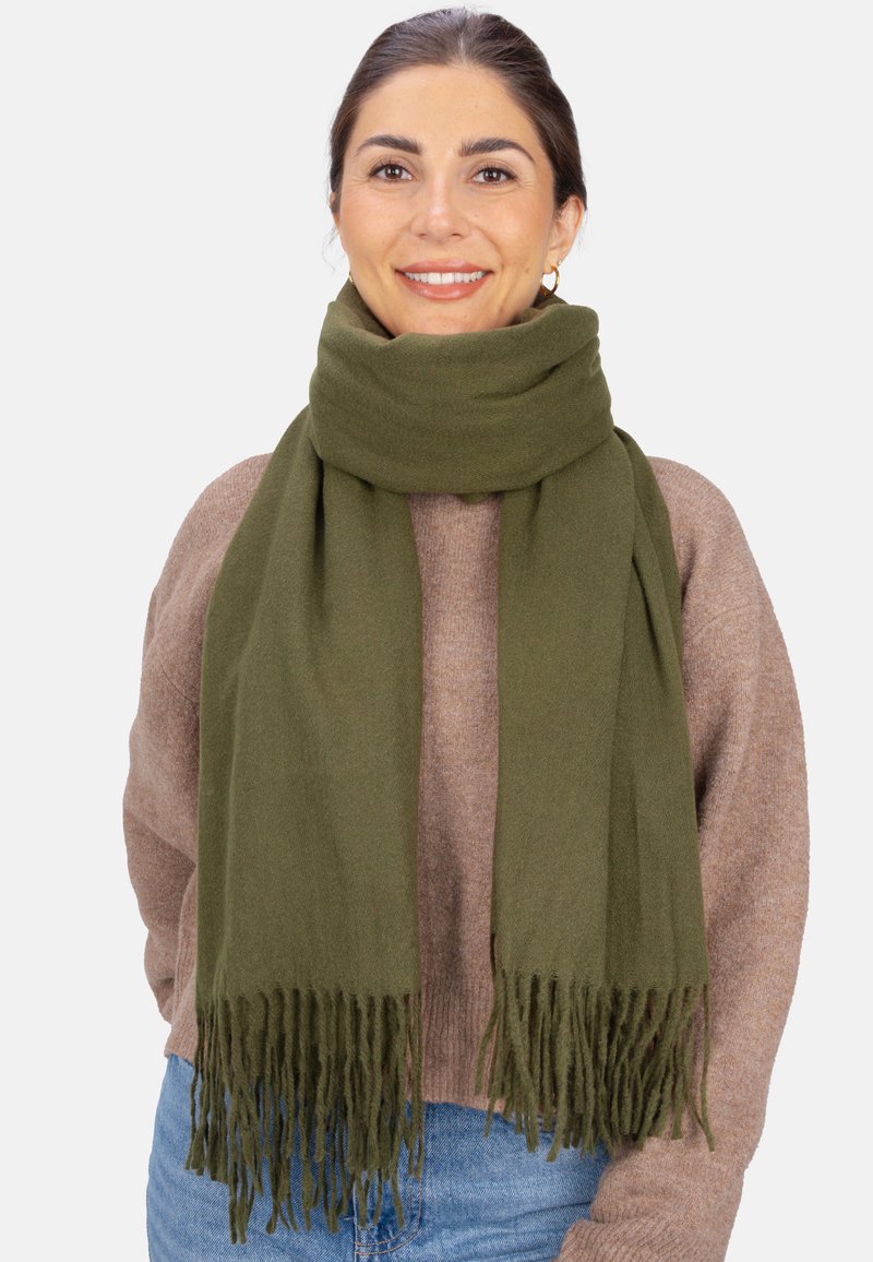 Écharpe vert olive en tissu doux avec bords frangés, drapée autour du cou, complétant un pull marron clair. Design minimaliste.